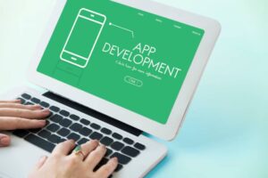 A person typing on a laptop with a bright green screen displaying 'App Development' and a phone illustration.