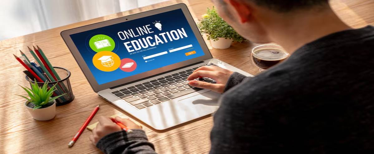 A person engages in online education on a laptop, with study materials and a coffee cup nearby, in a well-lit, cozy workspace.