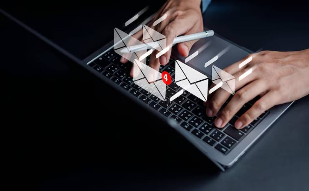 A pair of hands typing on a laptop keyboard with animated email icons and a notification for four new messages displayed.