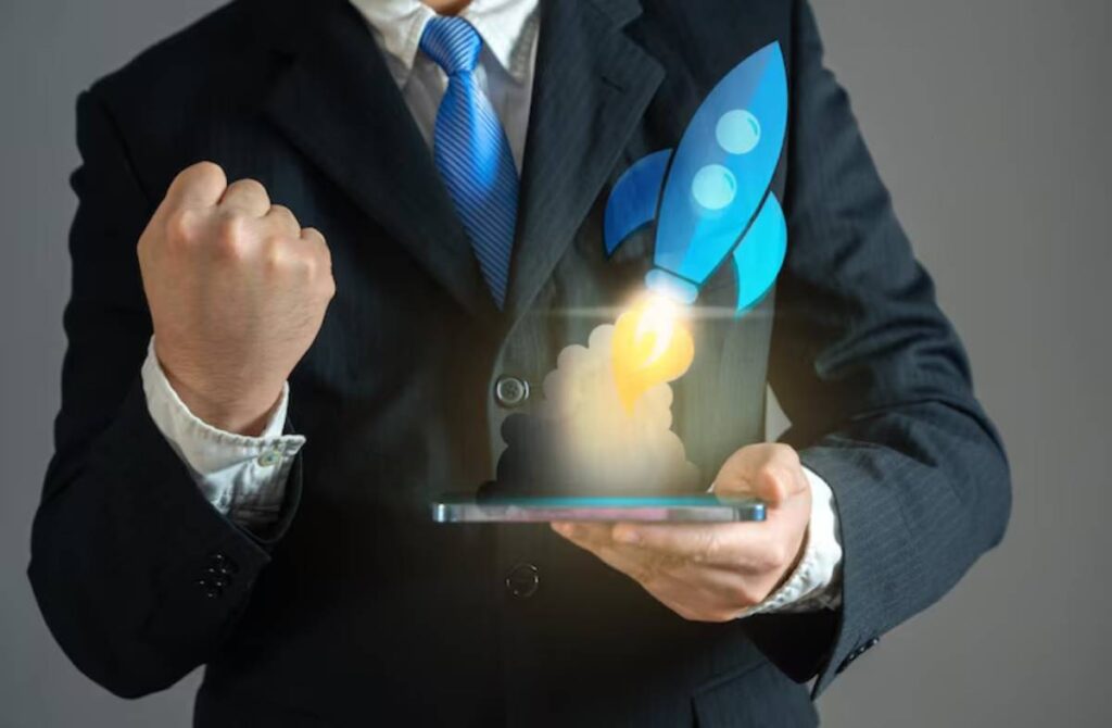 Businessman in a suit holds a smartphone with a launching rocket graphic, showing determination with a raised fist.