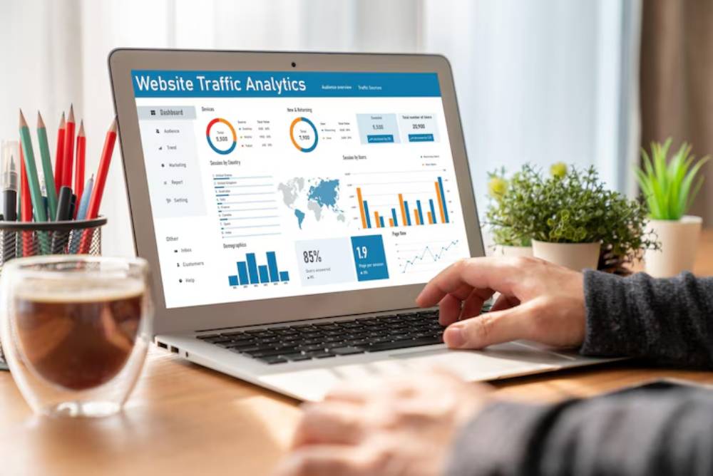 A person analyzes website traffic analytics on a laptop, showcasing graphs and data, with a cup of coffee and plants on the desk.