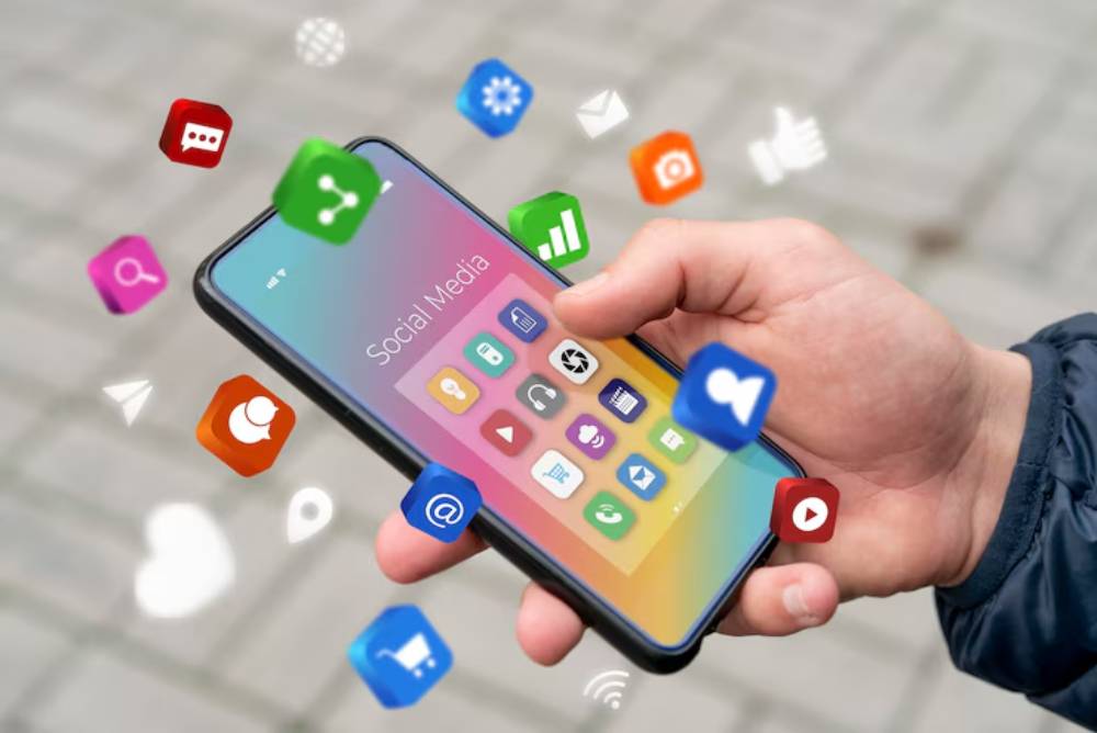 A hand holding a smartphone displaying a colorful social media interface with various app icons floating around it.
