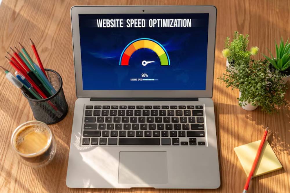 A laptop displays a 'Website Speed Optimization' graphic showing a 90% loading speed, surrounded by office supplies and coffee.