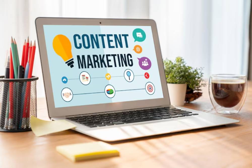 A laptop on a desk displays 'Content Marketing' with various related icons, surrounded by stationery, a coffee cup, and a small plant.