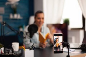 A cozy workspace featuring a person reading a book, a microphone, and a smartphone recording video content.