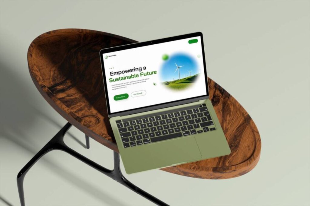 A green laptop displays a webpage about empowering a sustainable future, resting on a stylish wooden table.