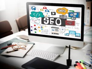 A computer screen displaying a colorful SEO and content strategy mind map, surrounded by office supplies on a desk.
