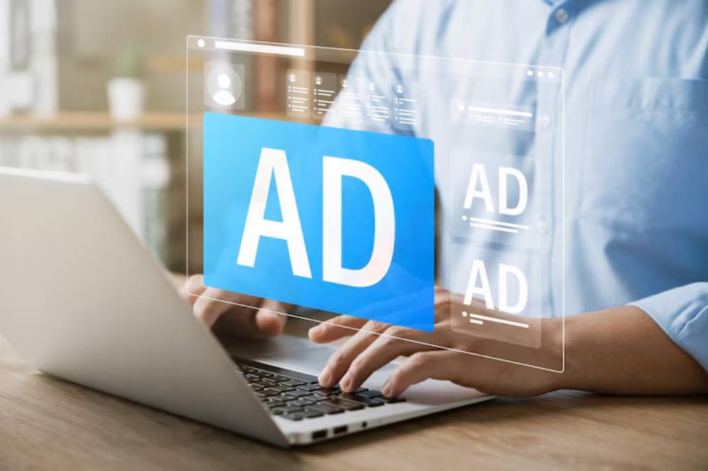 A person typing on a laptop with a transparent screen displaying the word 'AD' prominently in blue, representing digital advertising.