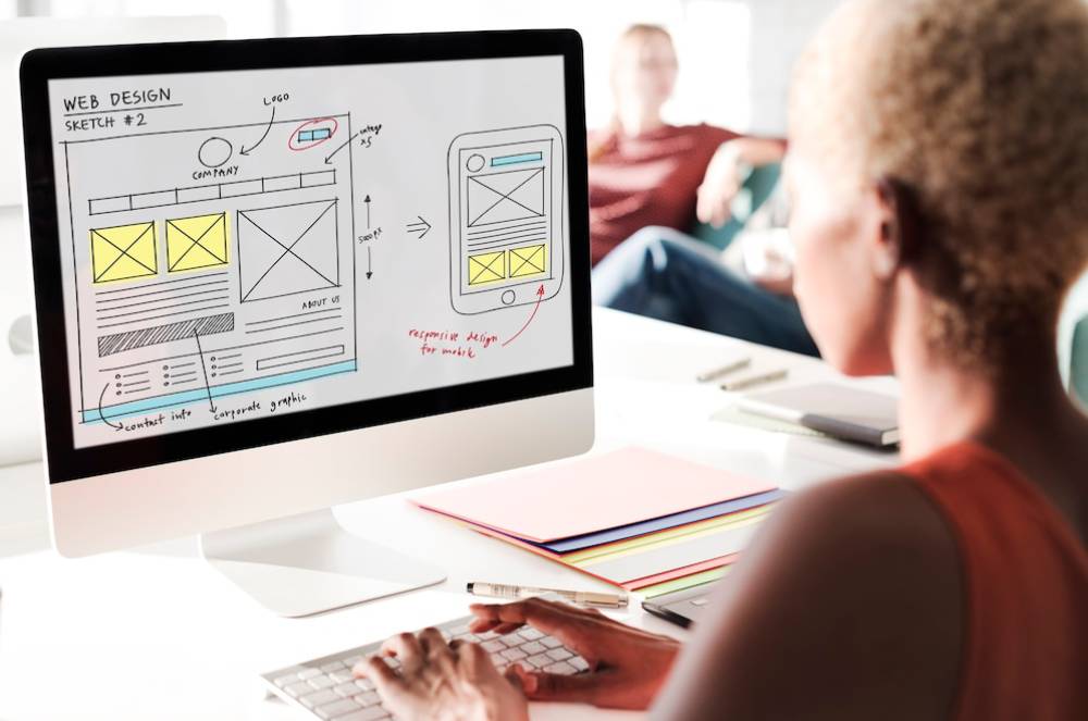 A person examines a web design sketch on their computer, showcasing layout ideas for both desktop and mobile views.